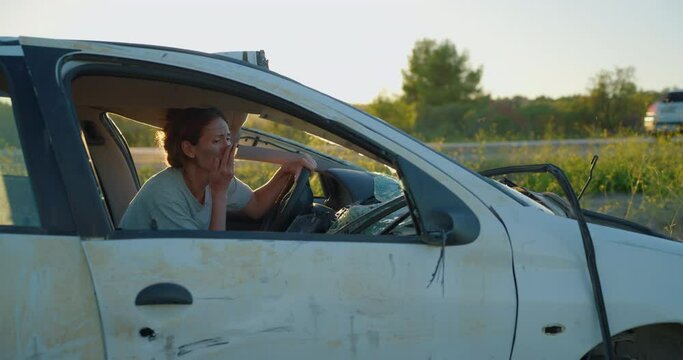 A curly-haired woman is stressed after being involved in a traffic accident on the highway. A woman sits in a broken car and leaves the vehicle