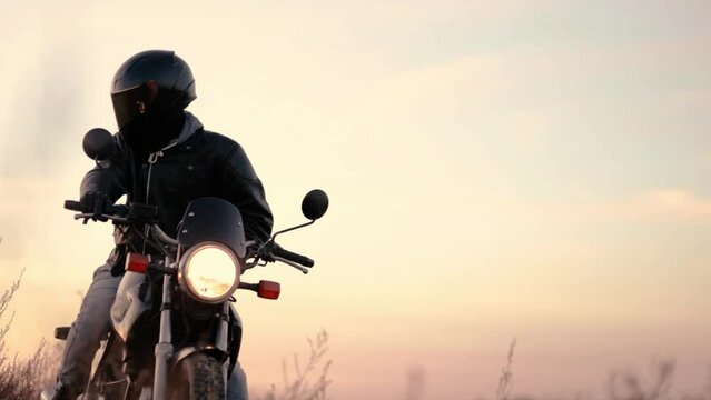 motorcyclist in a helmet and leather jacket at sunset with a classic motorcycle. Motorcycle life concept