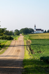 Fototapeta premium Looking down a country road lined with fields and a church on a sunny day in rural Minnesota, USA. 