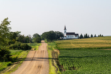 Looking down a country road lined with fields and a church on a sunny day in rural Minnesota, USA.
