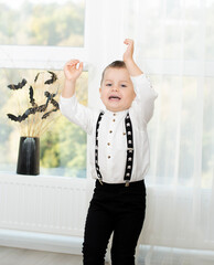 Halloween concept. Autumn holiday. A boy dances against the background of a window near a black vase with bats cut out of paper on dry branches. Close-up.