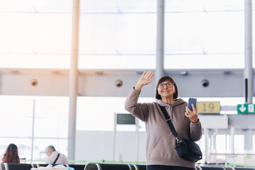 Happy smiling mature traveler woman hold smartphone and wave hand in greeting someone who meeting her at airport terminal after arrived from trip at new country at holiday vacation. Retirement travel © Andriy Medvediuk