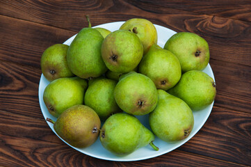 full plate of pears on a brown table. ripe pears on wooden background