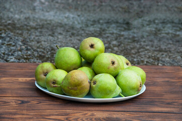 full plate of pears on a brown table. ripe pears on wooden background