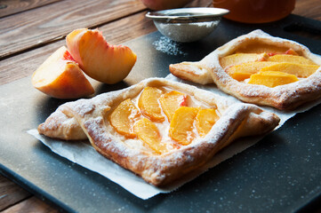 baking with peaches on the background of jam and peaches on the table. Sweet puff pastry with peaches, cream and powdered sugar.