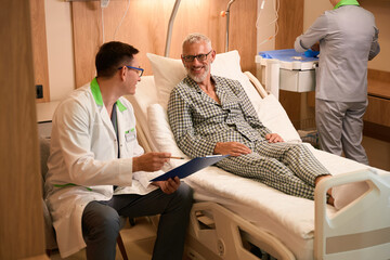 Old man in pajamas talks to attending physician in hospital room