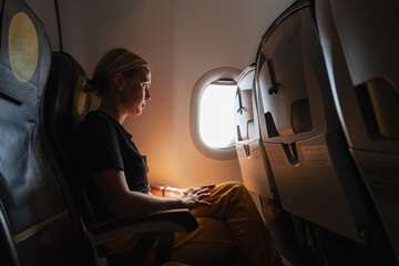 Passenger woman is flying in plane. Girl sitting in airplane looking out window going on trip...