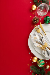 Transform your space: the road to a beautiful Christmas table. Top view vertical shot of cutlery, plates, glassware, fir twigs, tree ornaments, cones, stars confetti on red background with ad spot