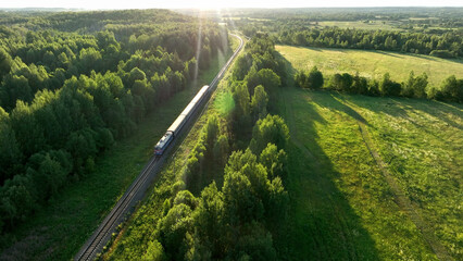 Train on railway in motion. Traveling on Passenger train on railway from forest, aerial view. Train with passenger cars rides. Drone view of an passenger locomotive with wagons in moving on railroad