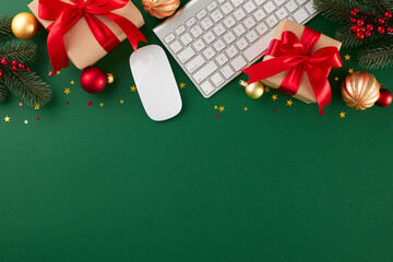 Embracing the ease of online Christmas gift shopping. Top view flat lay of computer mouse, keyboard, fir twigs, gift boxes, holiday baubles, gold stars on green background with advert area