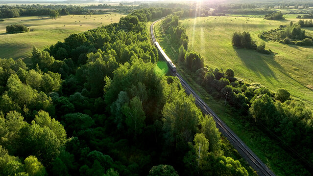 Train on railway in motion. Traveling on Passenger train on railway from forest, aerial view. Train with passenger cars rides. Drone view of an passenger locomotive with wagons in moving on railroad