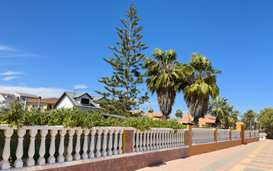 Fence with bushes and green garden at the villa. Exterior. Fence house at street with pavement road. Villa at seaside. Garden in luxury apartments. Fence and facade of house. House Exterior at coast.