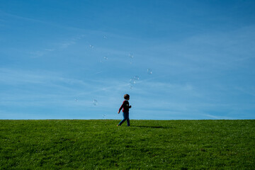 silhouette of a child on a hill playing with some soap bubbles in the sky