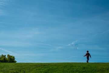 silhouette of a child on a hill playing with some soap bubbles