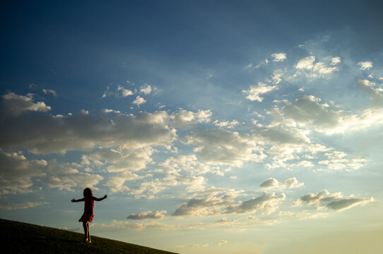the silhouette of a girl on a hill at sunset