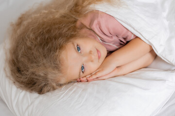 Fototapeta na wymiar Cute curly-haired girl sleeping in bed covered with a blanket