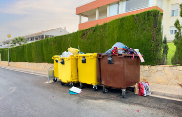 Naklejka premium Dumpster for Garbage and food waste on city Spain street. Plastic litter, packaging waste in garbage container. Trash and Household waste. Overcrowded garbage. Sorting, Full bins with Empty soda cans.