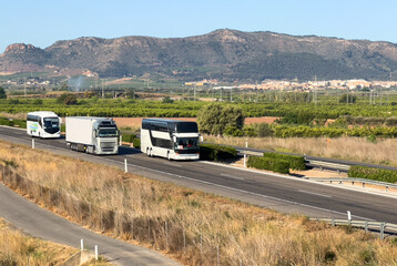 Semi truck and Tour Bus driving along highway. Goods Delivery by roads. Services and Transport logistics. Road traffic on motorway. Passenger bus on road. Bus travel in Europe. © MaxSafaniuk