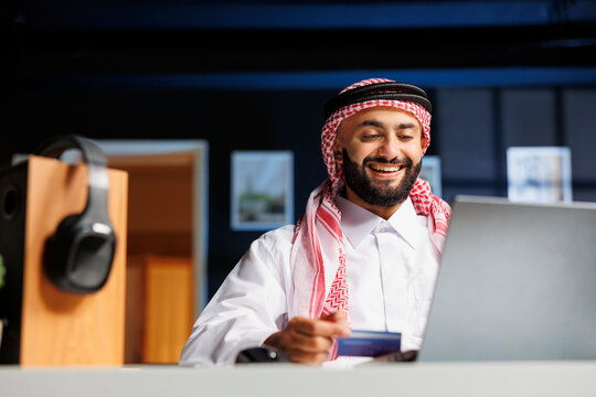 Arab businessman works diligently at a modern office desk, typing on his laptop. He browses the internet, communicates via email, and makes online payments with a credit or debit card.