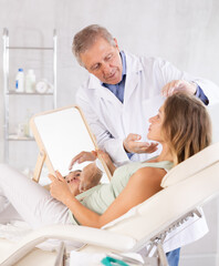 Obraz premium Middle-aged woman having consultation about face aesthetic with a specialist while looking in the mirror on clinical chair
