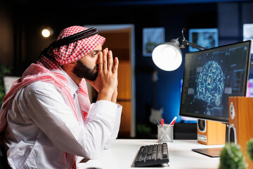 Arab man at desk uses advanced technology to develop secure software, utilizing AI, machine learning, and cloud computing. He ensures cyber security and works with code and programming.