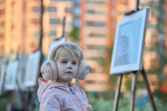 a child girl 5 years old on the street looks at photos of a street exhibition of photographers
