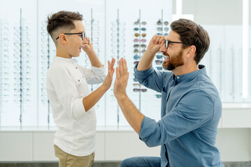 Portrait of happy attractive father and choosing and buying eyeglasses giving five high in optical...