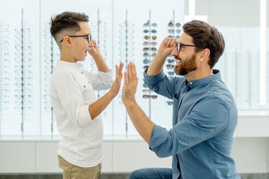 Portrait of happy attractive father and choosing and buying eyeglasses giving five high in optical store. Health care, vision concept 
