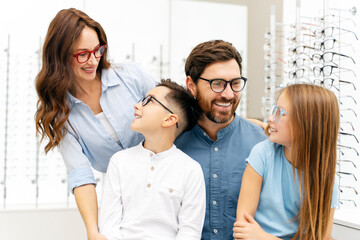 Young beautiful smiling family choosing glasses in modern optical store looking each other. Health...