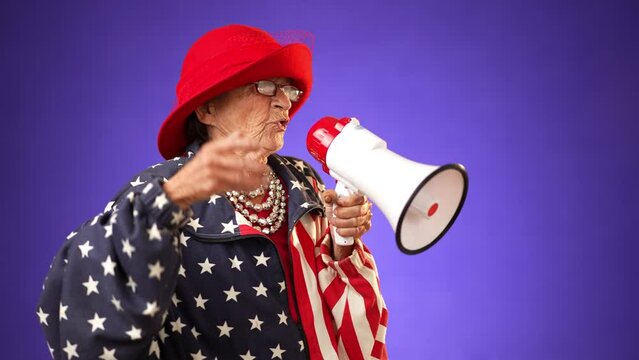 Funny toothless old elderly senior crazy grandmother woman yelling into megaphone bullhorn announcing something wearing US flag jacket with glasses, isolated on solid purple background