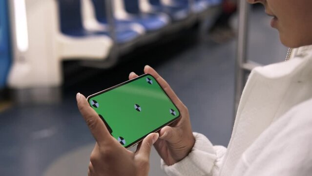 Woman using smartphone with horizontal green screen display watching content on train. Tracking markers. Girl in subway using smart phone internet surfing communication online. Public transport. 4K