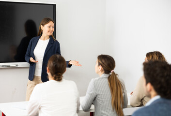 Friendly businesswoman standing near interactive board and communicating with group of adult...