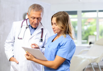 Two fellow doctors, adult woman and senior man, standing in medical office with papers in hands, focused on discussing of clinical diagnosis of patient - obrazy, fototapety, plakaty