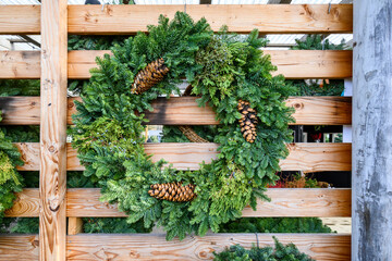 Fresh Christmas wreath made out of live evergreen branches and pine cones hanging on a rustic wood wall, Christmas holiday decoration
 - Powered by Adobe