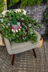 Holliday scene with a holiday troll sitting on a modern chair surrounded by leafy greens
