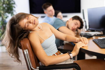 Tired young female employee engaged in programming or data analysis in coworking space dozing off...