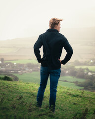 A man looks back and enjoys the view after a long hike up a hill - obrazy, fototapety, plakaty
