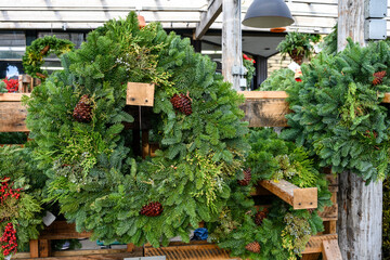 Fresh Christmas wreaths made out of live evergreen branches and pine cones for sale in a covered outdoor nursey, Christmas holiday decoration
