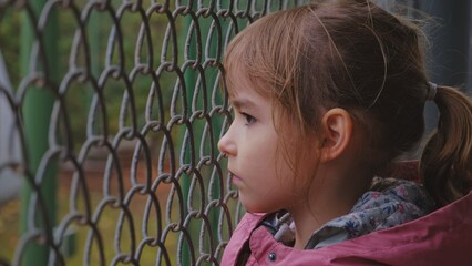 Sad Beautiful Young Caucasian Girl Looking through Wire Fence at School Backyard or Refugee Camp