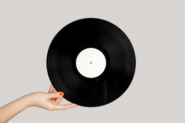 Closeup of woman hand showing retro spinning music plate for gramophone. Indoor studio shot isolated on gray background.