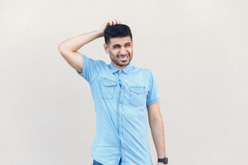 Portrait of puzzled confused pensive young adult man wearing denim shirt standing with hand on...
