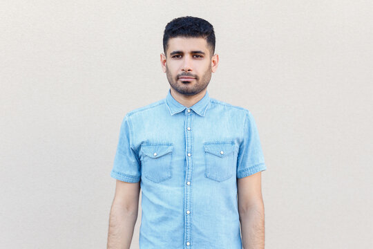 Portrait of attractive serious concentrated man wearing denim shirt standing looking at camera, looks strict and self-confident. Indoor studio shot isolated on gray background.