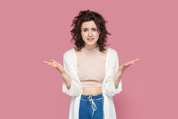 Portrait of angry attractive young adult woman with curly hair wearing casual style outfit raised her hands, asking what, arguing, frowning face. Indoor studio shot isolated on pink background. - obrazy, fototapety, plakaty