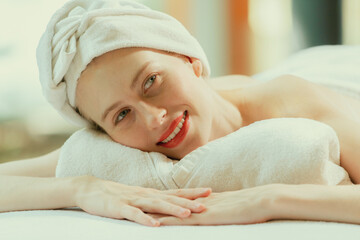 Fototapeta na wymiar A beautiful young woman lies on a spa bed, her body relaxed and at peace. Pretty caucasian girl surrounded by the spa environment and the gentle aroma of essential oils. Close up. Tranquility.