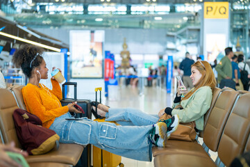 Young woman passengers with suitcase using mobile phone booking hotel during waiting flight at boarding gate in airport terminal. Attractive girl tourist travel by airplane on holiday vacation. - obrazy, fototapety, plakaty