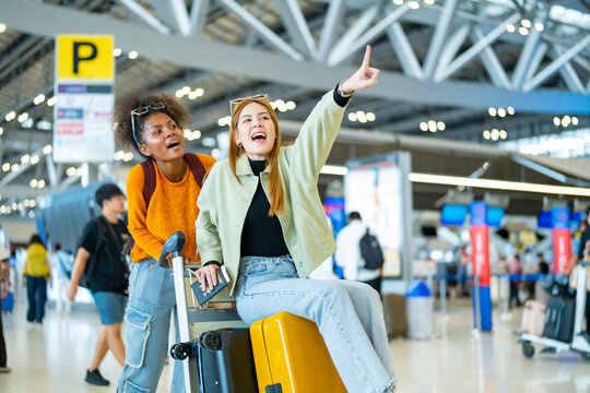 Happy woman friends holding passport and luggage walking together to airline check in counter in airport terminal. Attractive girl enjoy and fun travel on holiday vacation with airplane transportation