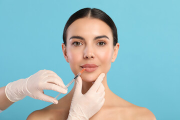 Doctor giving lips injection to young woman on light blue background. Cosmetic surgery
