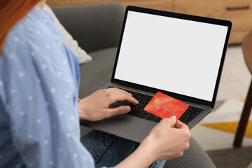 Woman with credit card using laptop for online shopping on sofa indoors, closeup