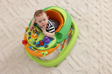 Cute baby making first steps with toy walker on soft carpet, above view. Space for text - obrazy, fototapety, plakaty