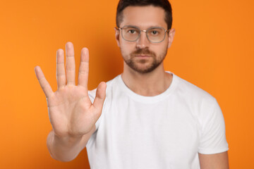 Fototapeta premium Handsome man showing stop gesture on orange background, selective focus